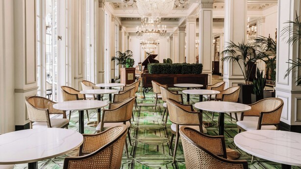A hotel lobby with a long corridor, round tables, wicker chairs, a large chandelier, and a green patterned carpet. - The St. Anthony, A Luxury Collection Hotel, San Antonio (San Antonio)
