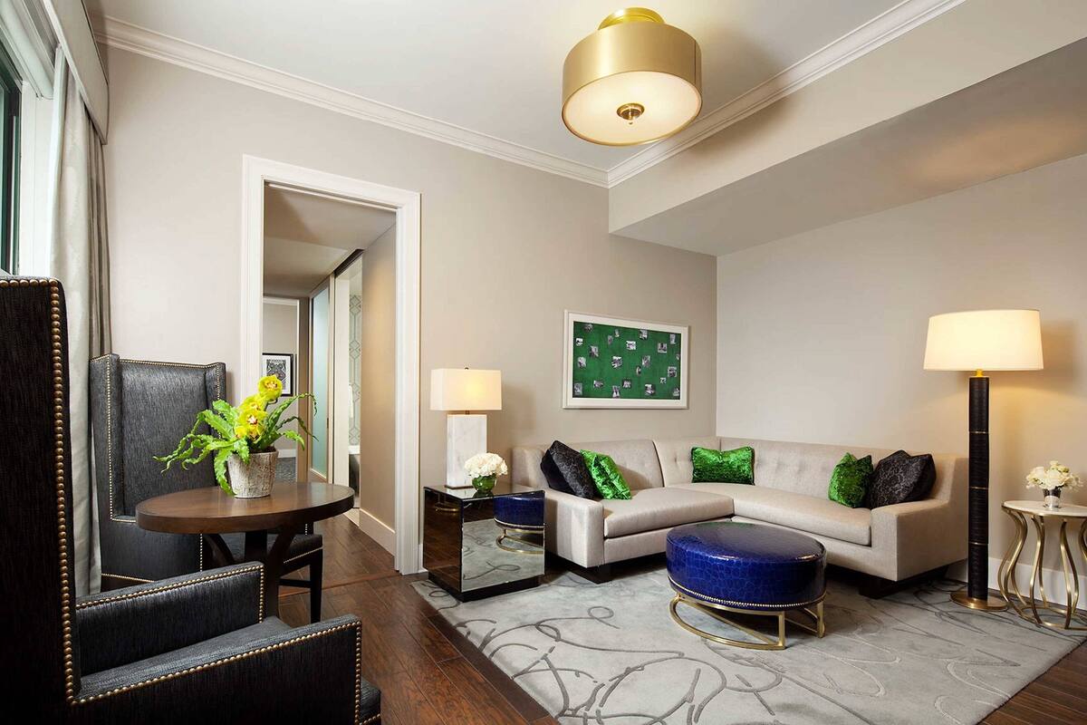 A modern living room with a sofa, ottoman, and chairs, a dining table with a plant, and a large mirror.