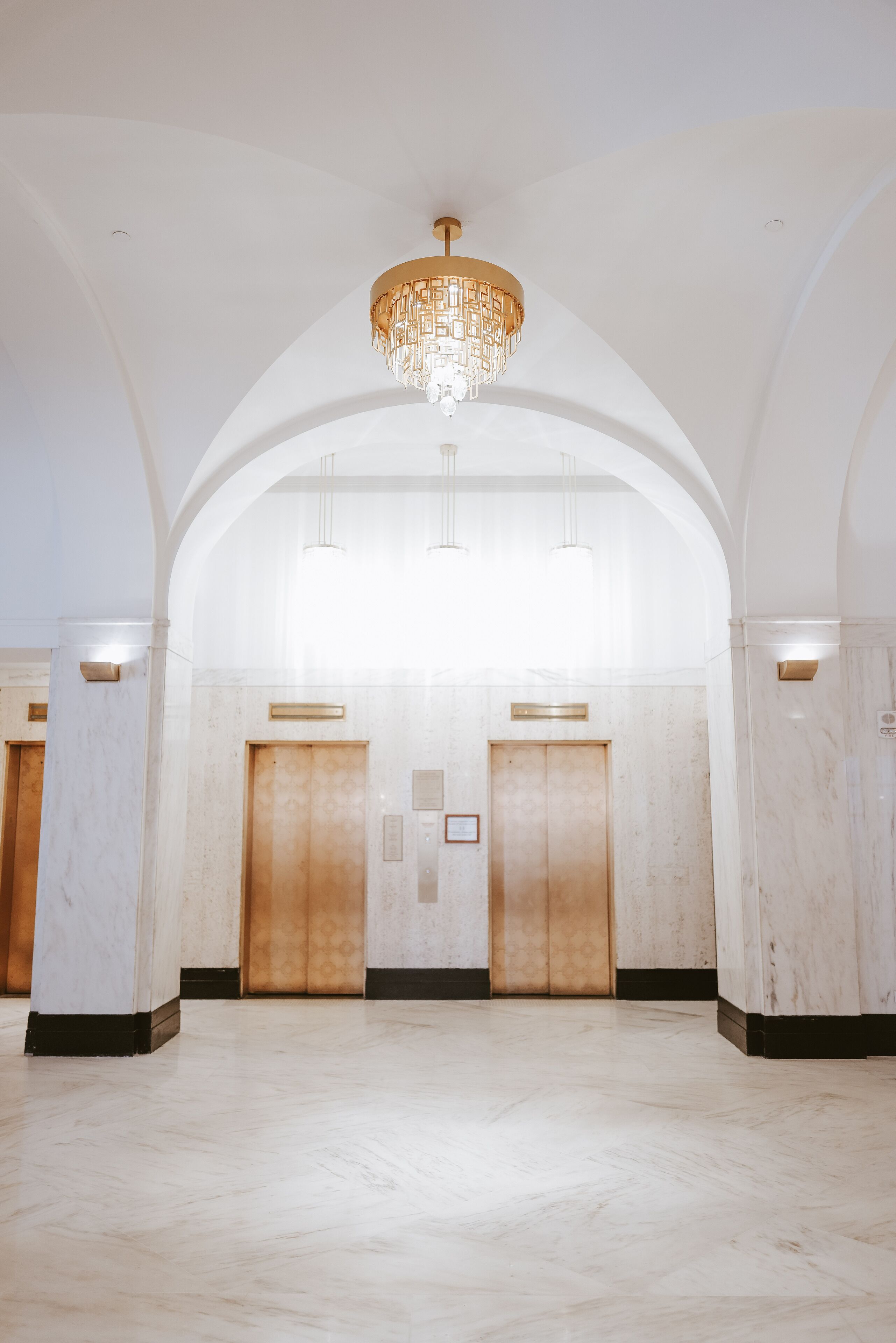 A spacious lobby with marble flooring, two elevators, and a chandelier.
