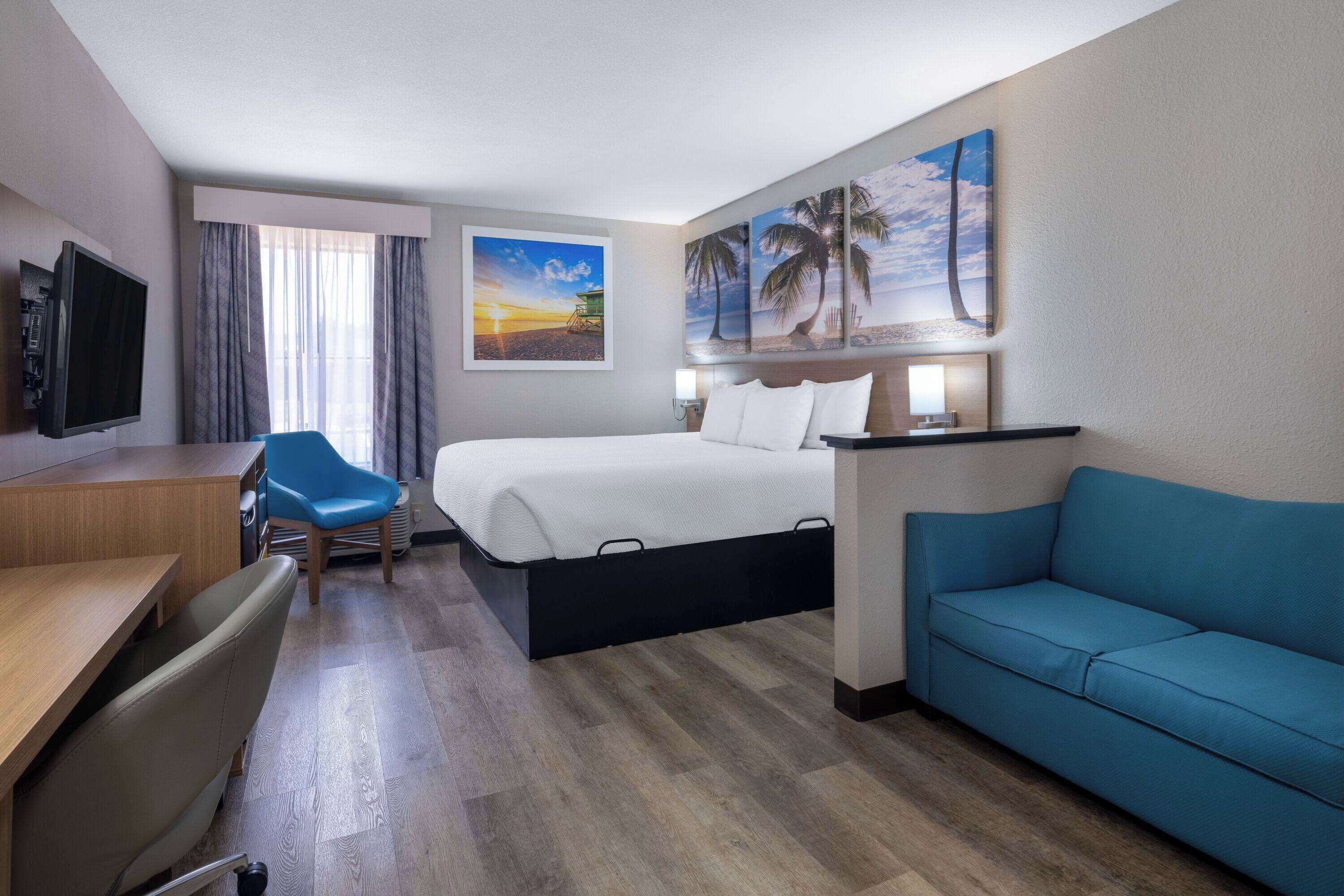 A hotel room with a bed, a desk, a blue chair, a sofa, and artwork on the walls.