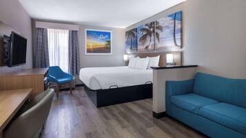 A hotel room with a bed, a desk, a blue chair, a sofa, and artwork on the walls.