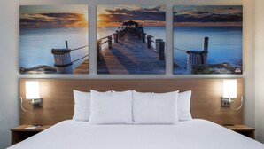 A hotel room with a large bed, two bedside tables with lamps, and a wall with three paintings of a pier and sunset. - Days Inn & Suites by Wyndham Commerce (Commerce)