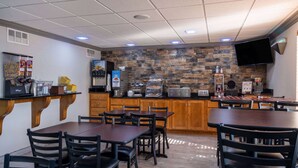 A restaurant with wooden tables and chairs, a stone wall, and a flat-screen TV mounted on the wall. - Days Inn & Suites by Wyndham Commerce (Commerce)