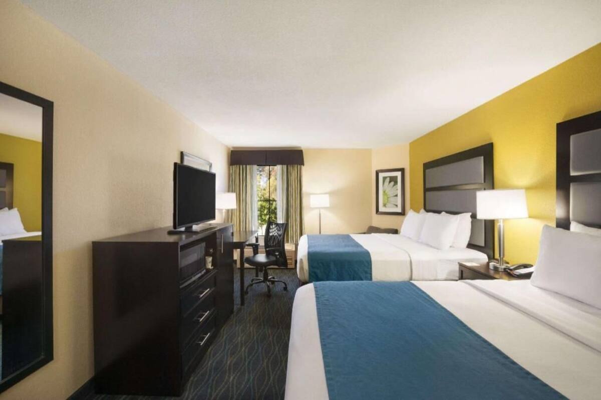 Quarto de hotel com duas camas, uma escrivaninha, uma televisão e uma janela com cortinas.