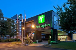 Un hotel Holiday Inn con diseño moderno, que presenta un logo verde llamativo, una escalera que conduce a la entrada y una fachada bien iluminada.