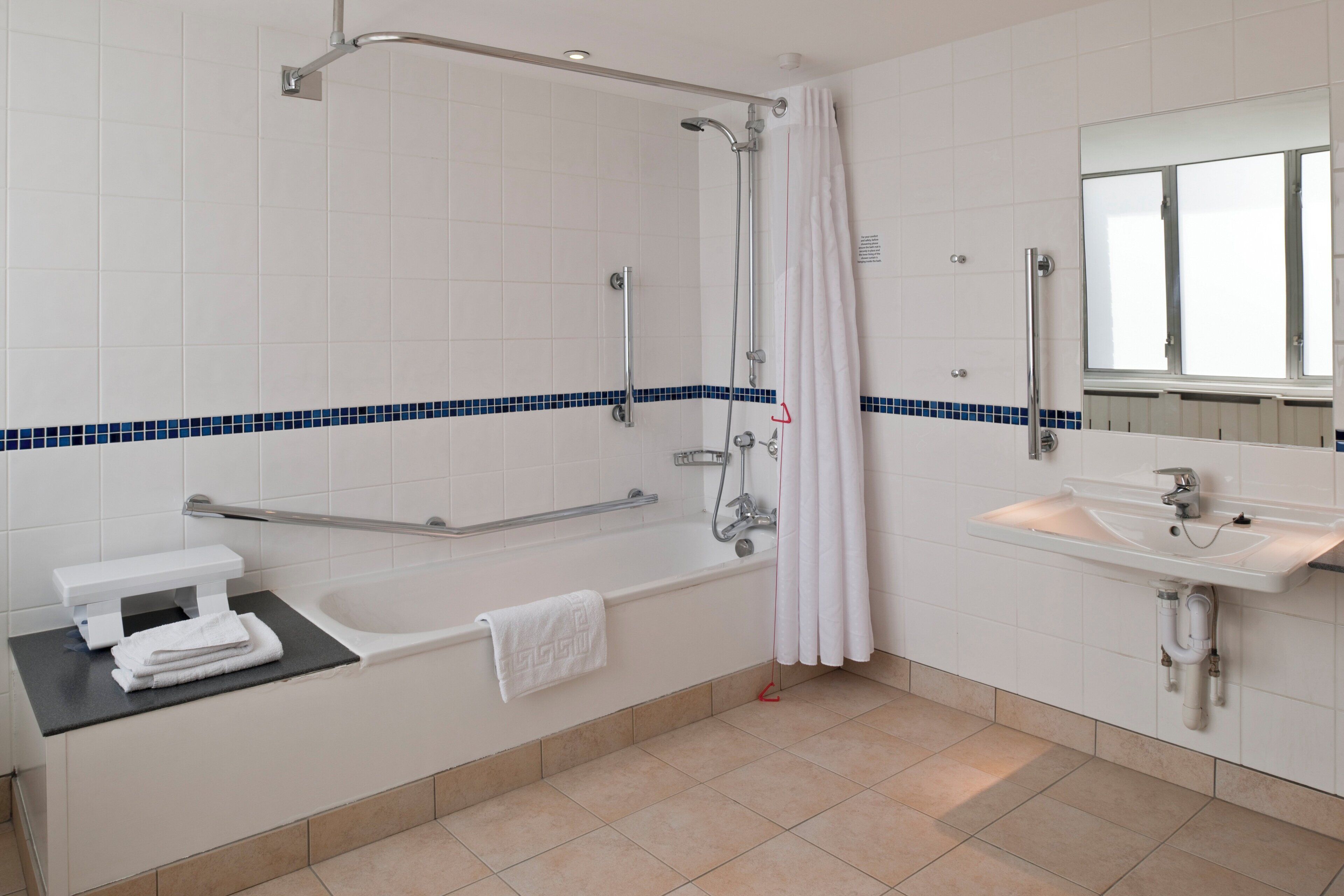 Un baño con bañera, ducha, lavabo y barra de apoyo.