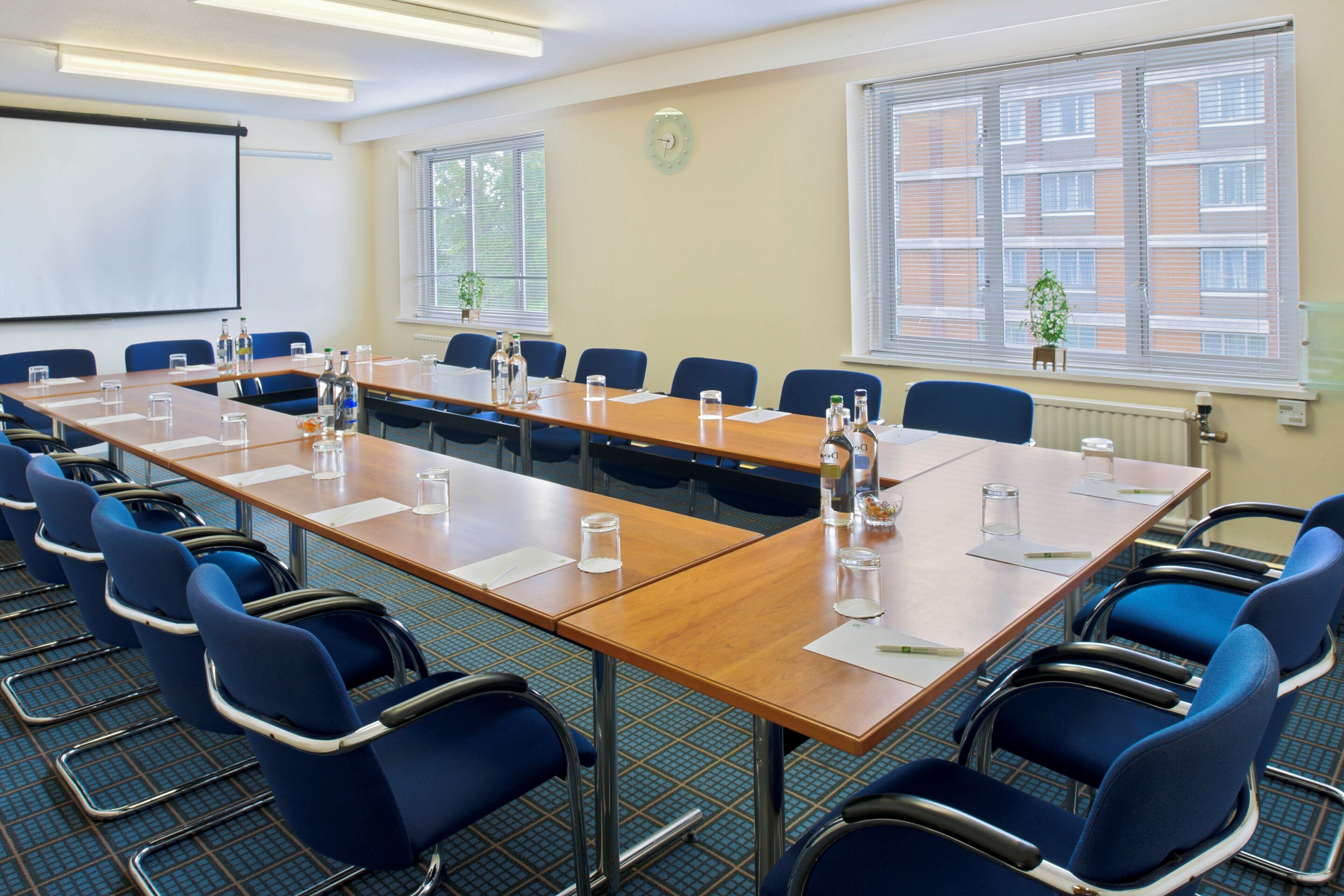 A conference room with a long table, blue chairs, and a projector screen.