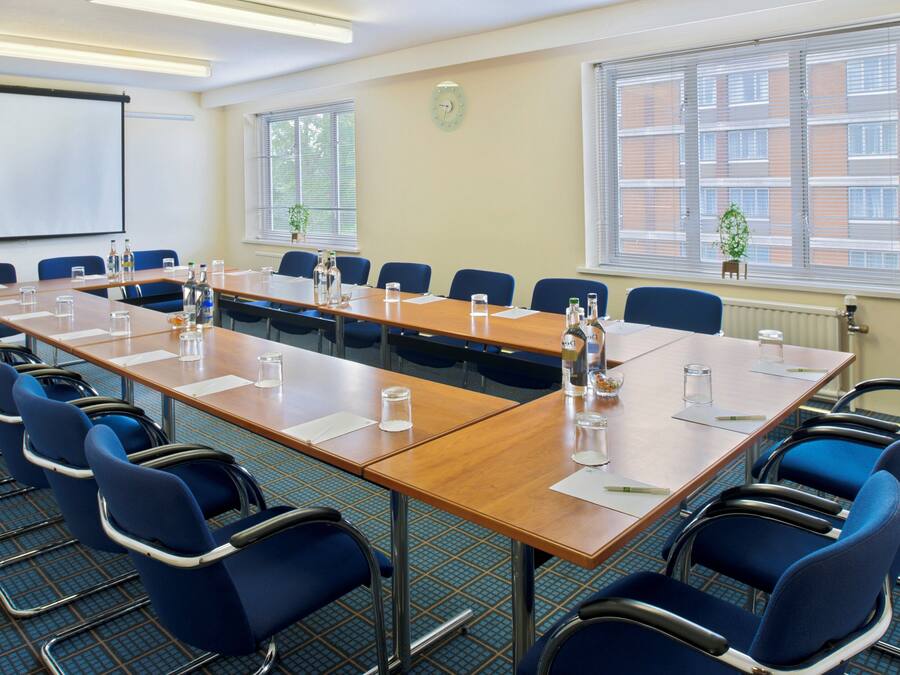 A conference room with a long table, blue chairs, and a projector screen.