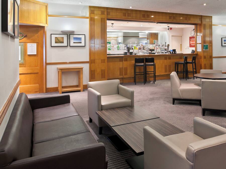 Un vestíbulo de hotel con disposición de asientos, zona de bar y mostrador de recepción.