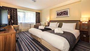 A hotel room with two beds, a desk, a TV, and a window with curtains.