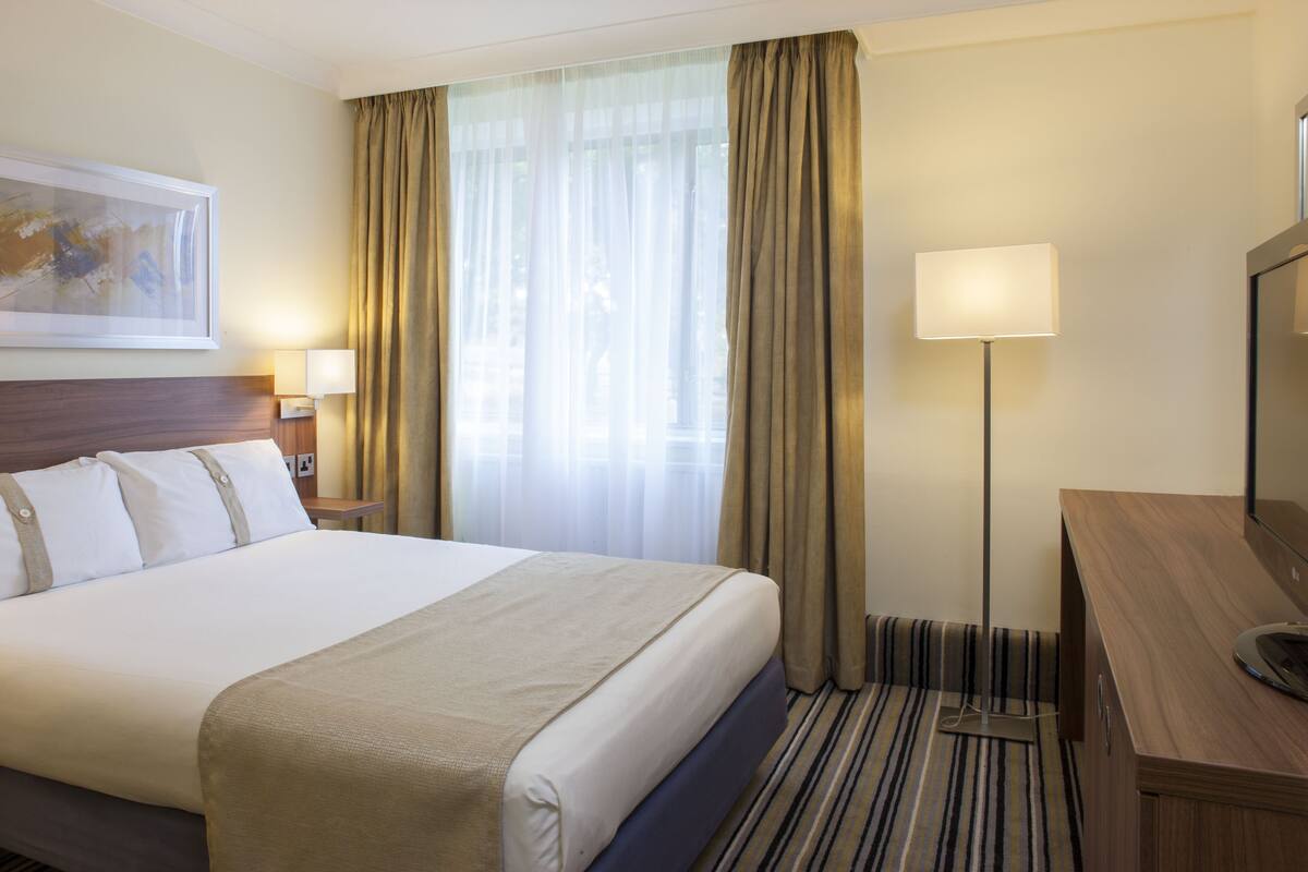 Ett hotellrum med en stor säng, ett skrivbord, en lampa och en tavla på väggen.