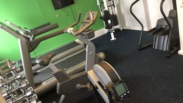 Une salle de sport équipée de divers appareils, notamment un tapis de course, un vélo d’appartement et un appareil elliptique.