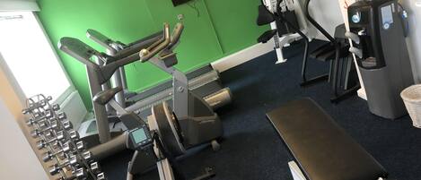 Une salle de sport équipée de divers appareils d’exercice, notamment des tapis de course, des appareils de musculation et des haltères.