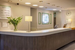 A hotel reception desk with a white counter, a clock, and a framed picture on the wall. - Holiday Inn Washington by IHG (Washington)