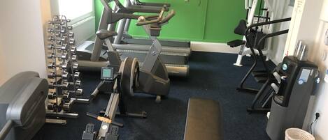 Ein Fitnessstudio mit Cardiogeräten, Gewichten und einer Bank.