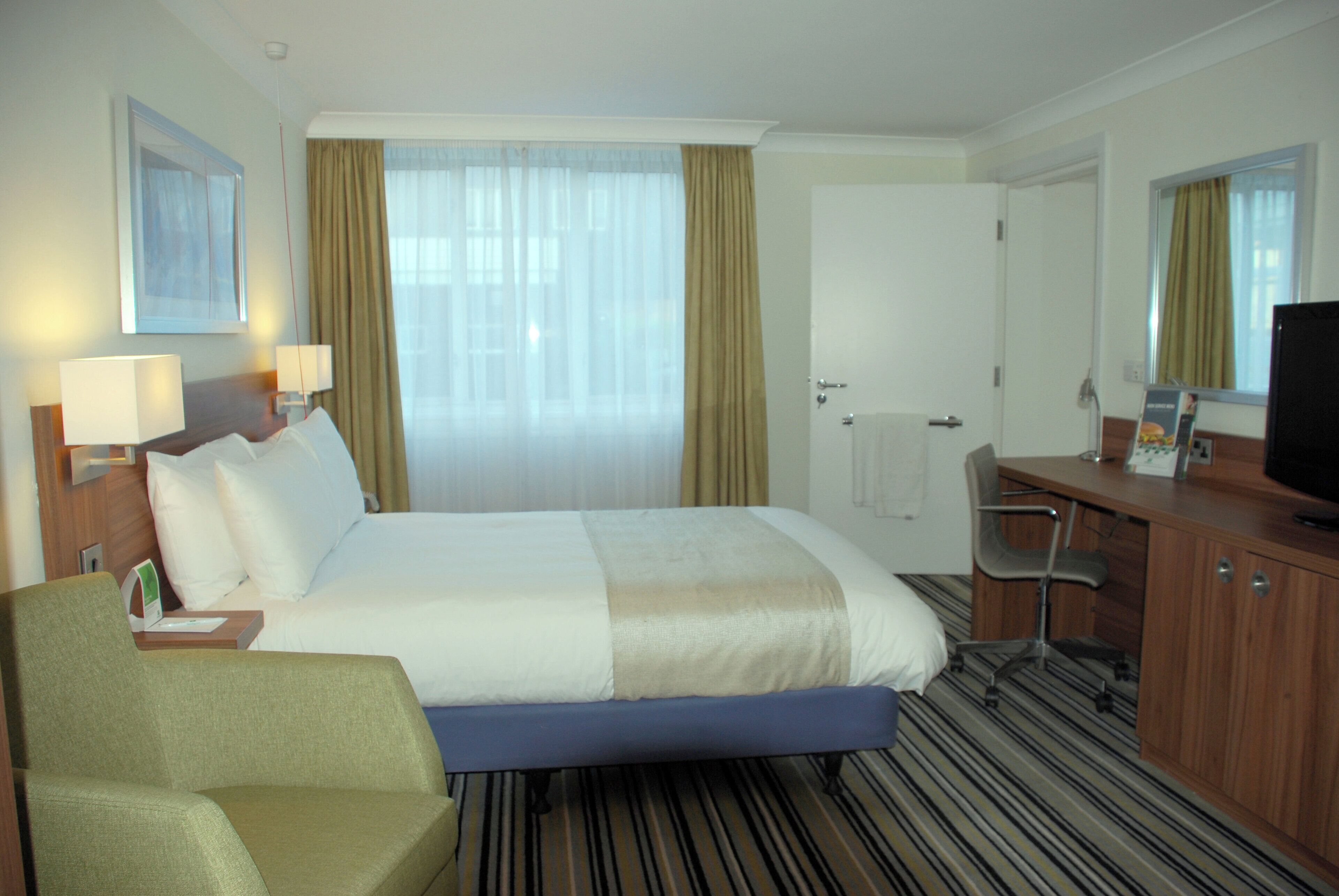 A hotel room with a bed, a desk, a chair, a television, and a window with curtains.