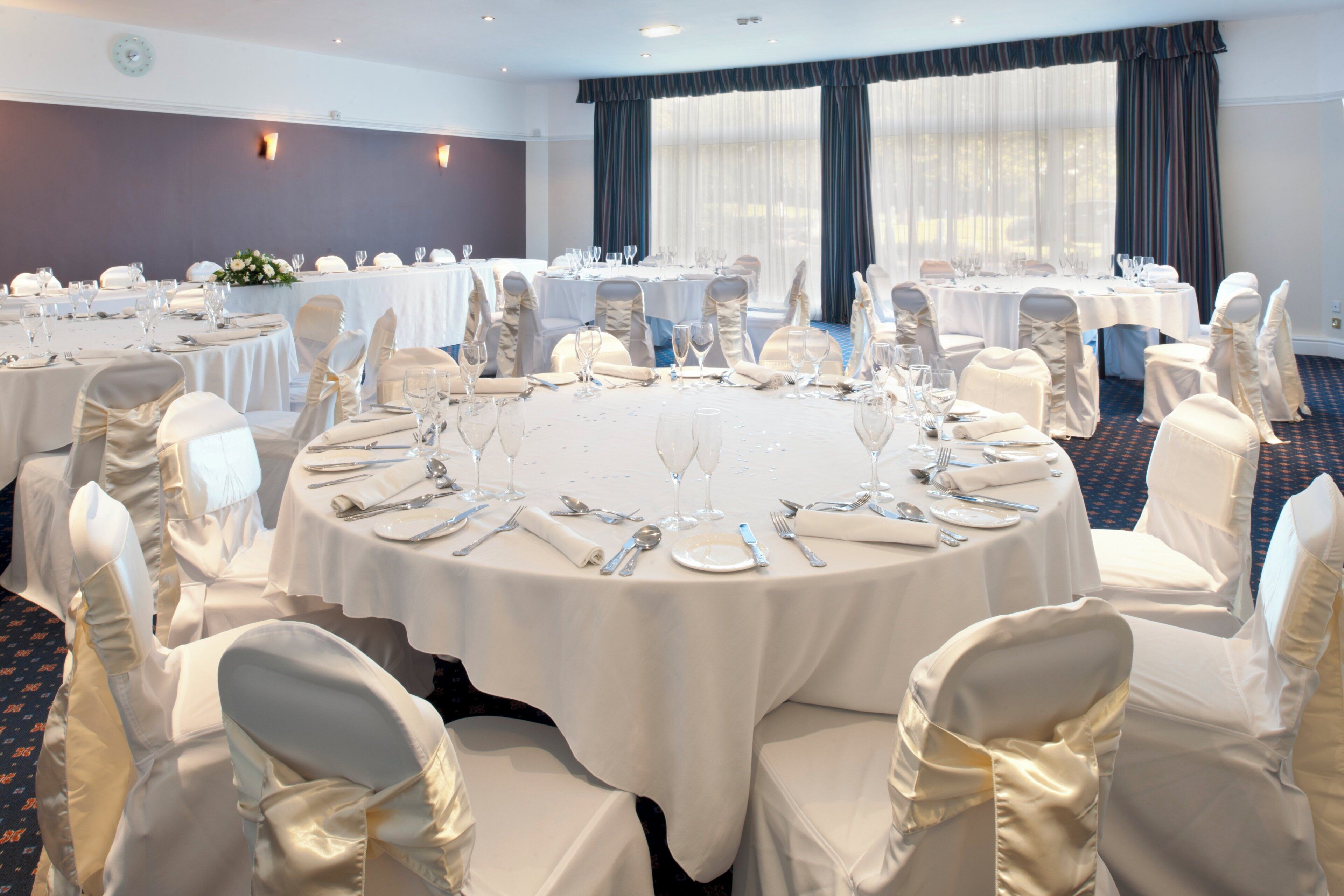 A conference room with round tables, white tablecloths, and chairs with white covers.
