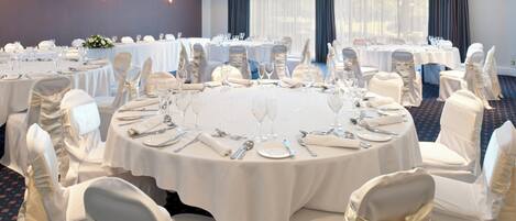 A conference room with round tables, white tablecloths, and chairs with white covers.