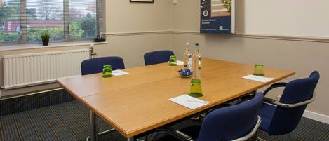A conference room with a wooden table, blue chairs, and green glass candle holders.