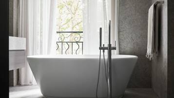 A modern bathroom with a freestanding bathtub, a towel rack, and a view through a window with a balcony.