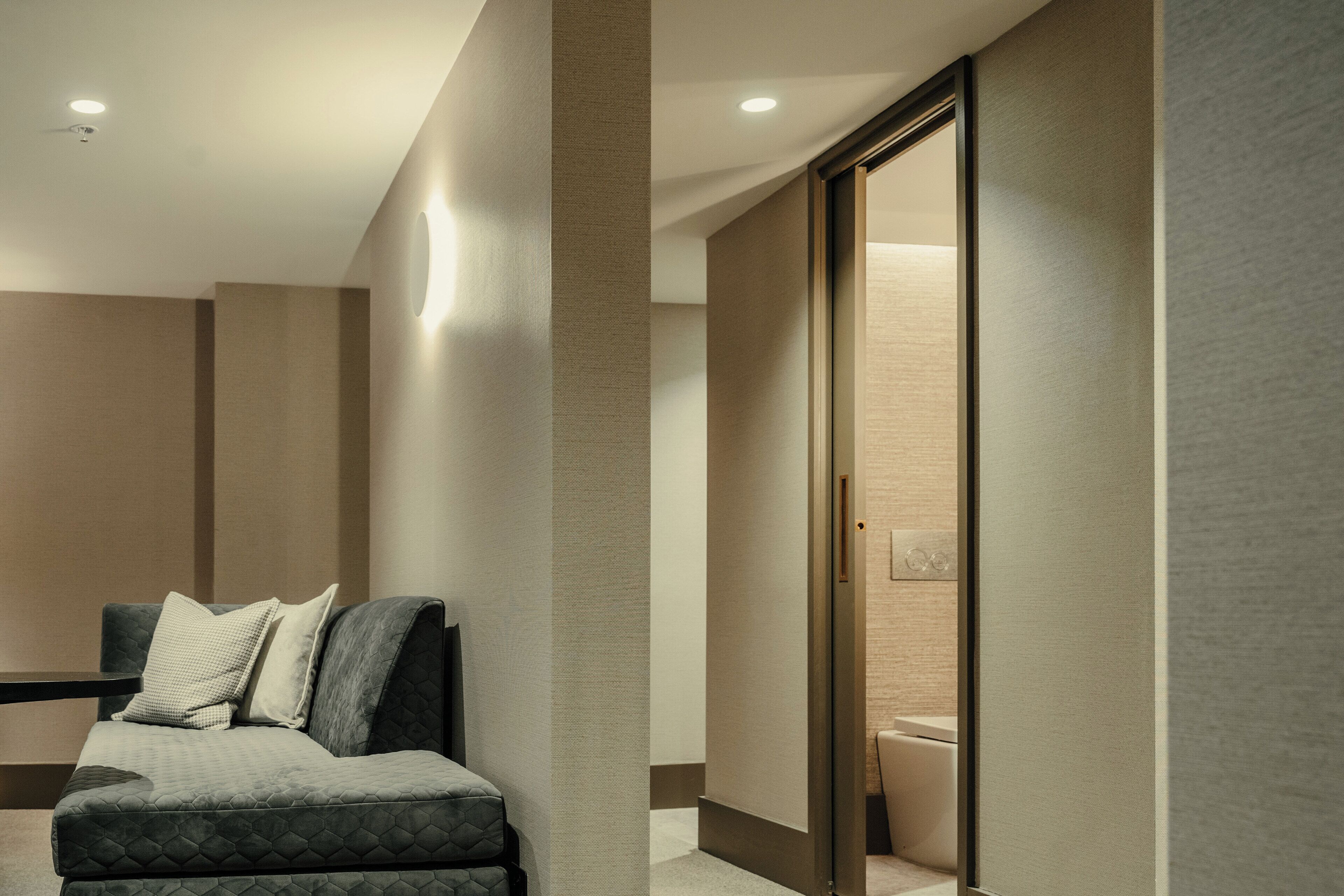 A modern hotel room with a sofa, a glass partition, and a visible bathroom.