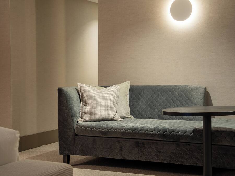 A modern room with a grey quilted sofa, a round table, and a wall-mounted light fixture.