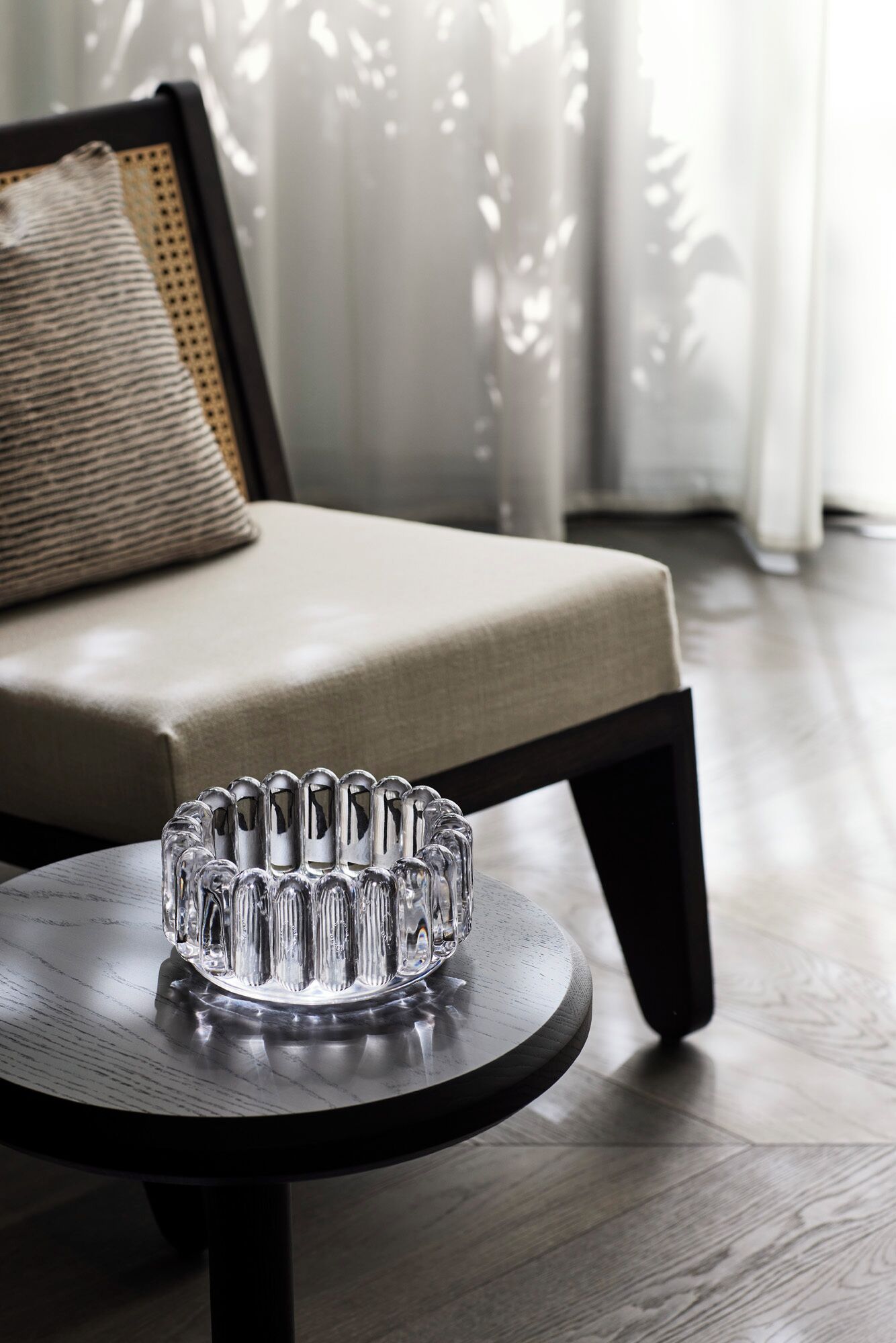 A round table with a clear glass object on it, a sofa with a woven cushion, and a wooden floor.