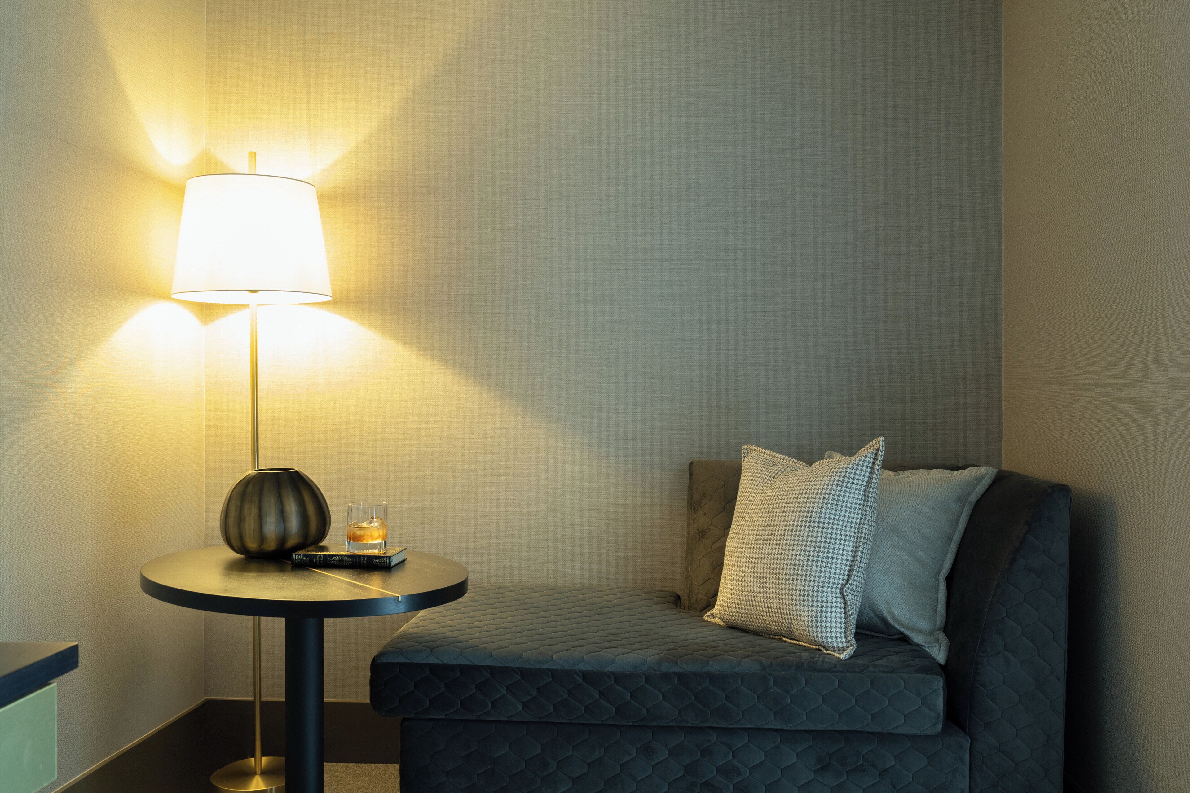 A corner of a room with a round table, a lamp, and a sofa with cushions.