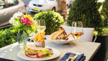 A table set with a sandwich, fries, a glass of white wine, and a vase of flowers.