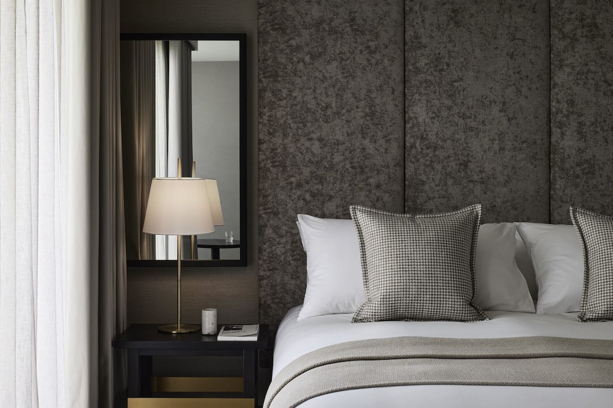 A neatly made bed with white linens and patterned pillows, a bedside lamp, and a small table with a book and a candle.