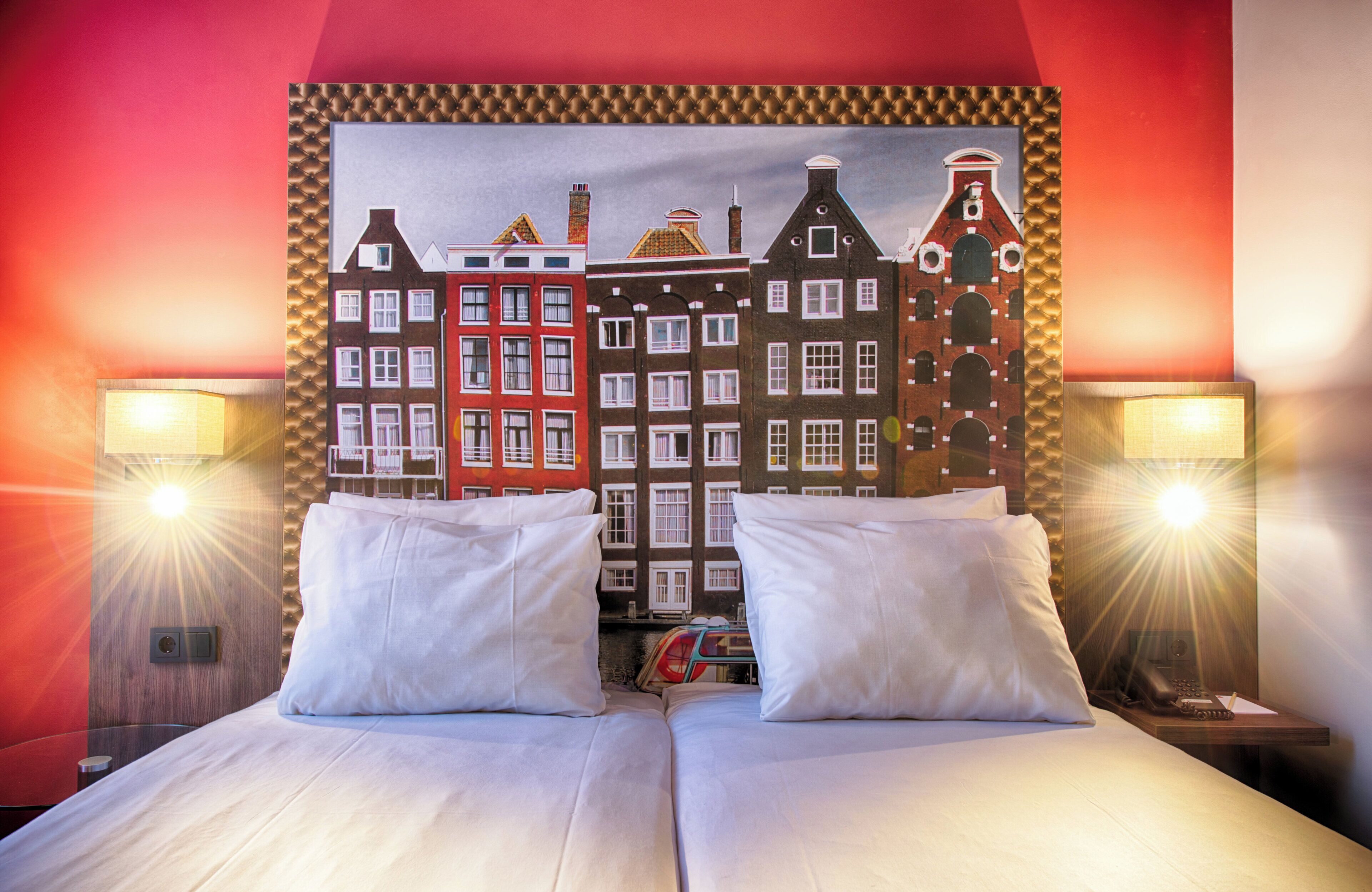 Een hotelkamer met een bed, twee nachtkastjes en een schilderij van Europese gebouwen.