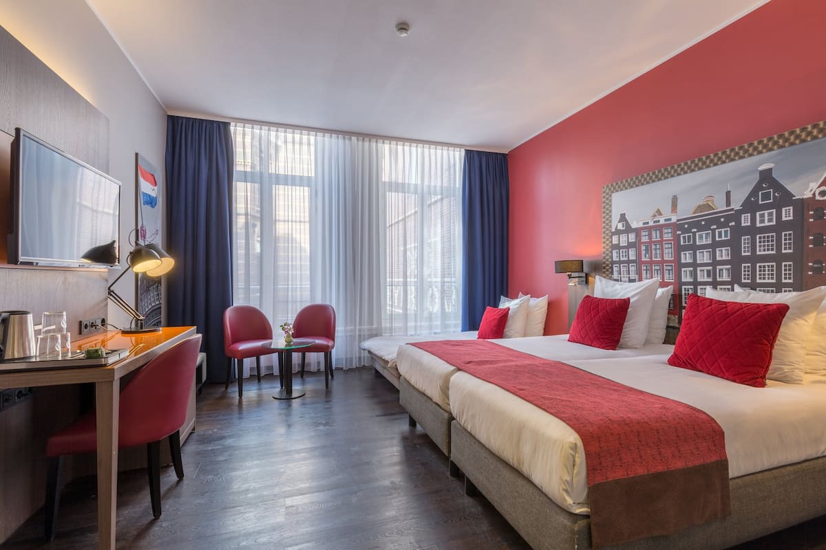 A hotel room with a bed, desk, chairs, and a large window.