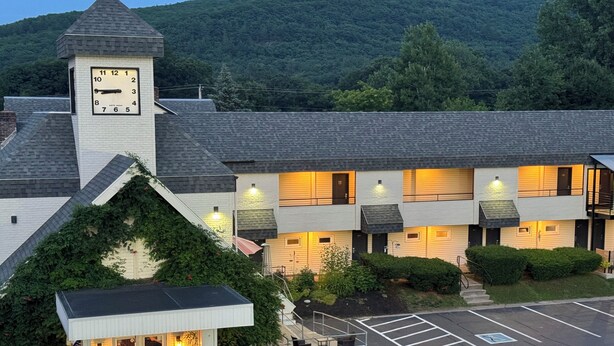A hotel with a clock tower, a parking lot, and a well-maintained garden. - Black Mountain Inn (Brattleboro)