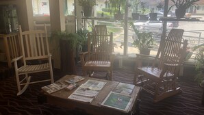 A cozy reading area with wooden chairs, a table with newspapers, and potted plants. - Black Mountain Inn (Brattleboro)