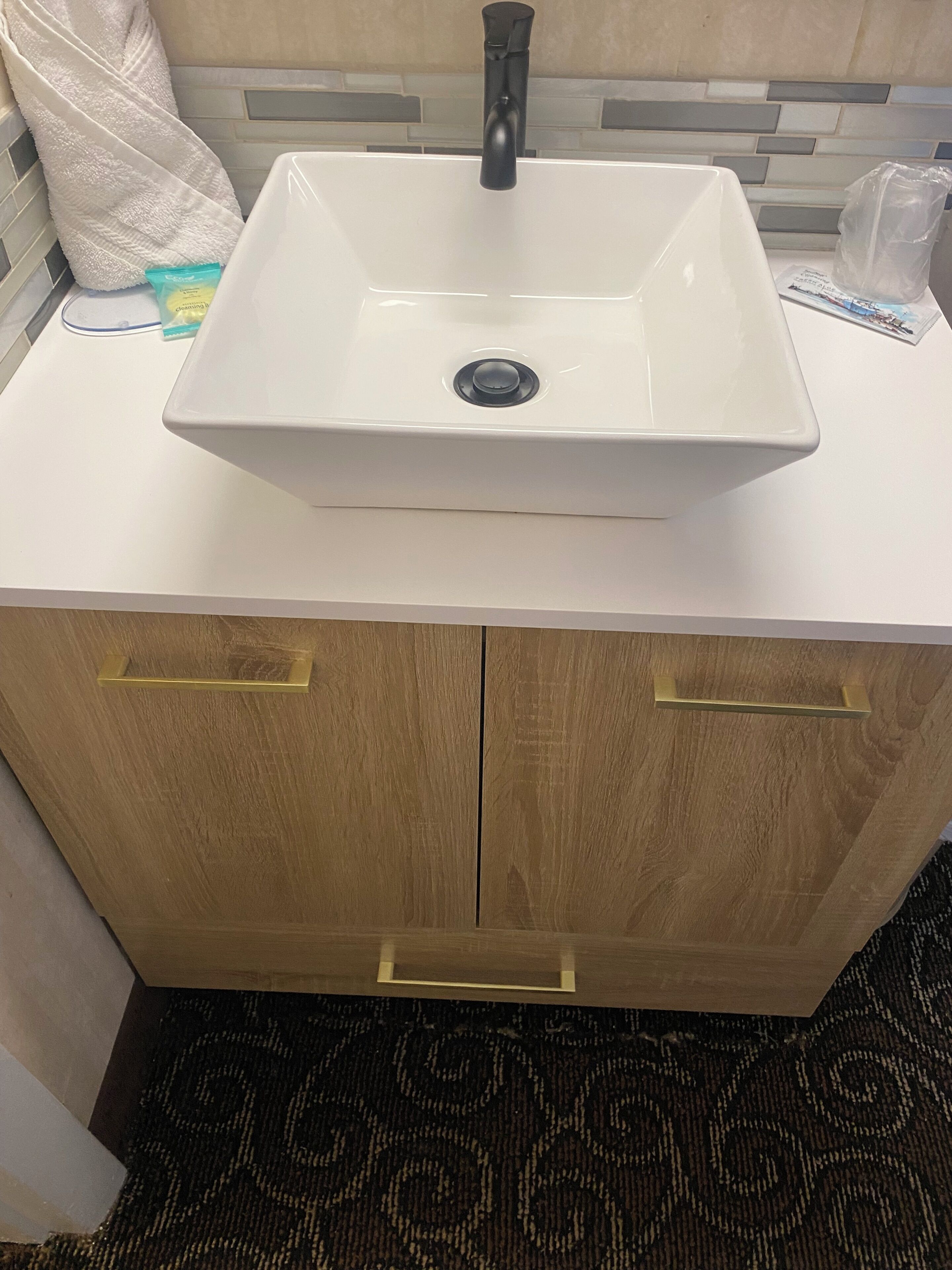 A bathroom with a white sink, wooden cabinets, and a patterned carpet.