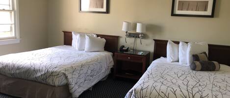 A hotel room with two beds, a nightstand, a lamp, and framed pictures on the wall.