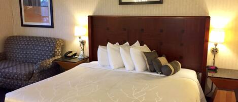 Une chambre d’hôtel avec un grand lit, une chaise, une table de chevet avec un téléphone et une lampe, et des tableaux encadrés au mur.