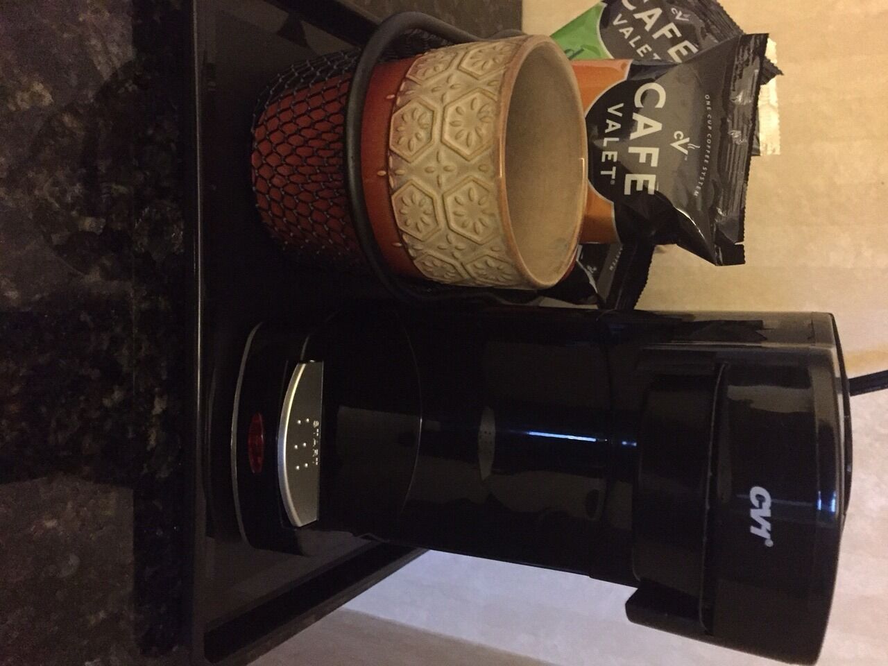 A coffee maker, a patterned mug, and a coffee bag on a countertop.