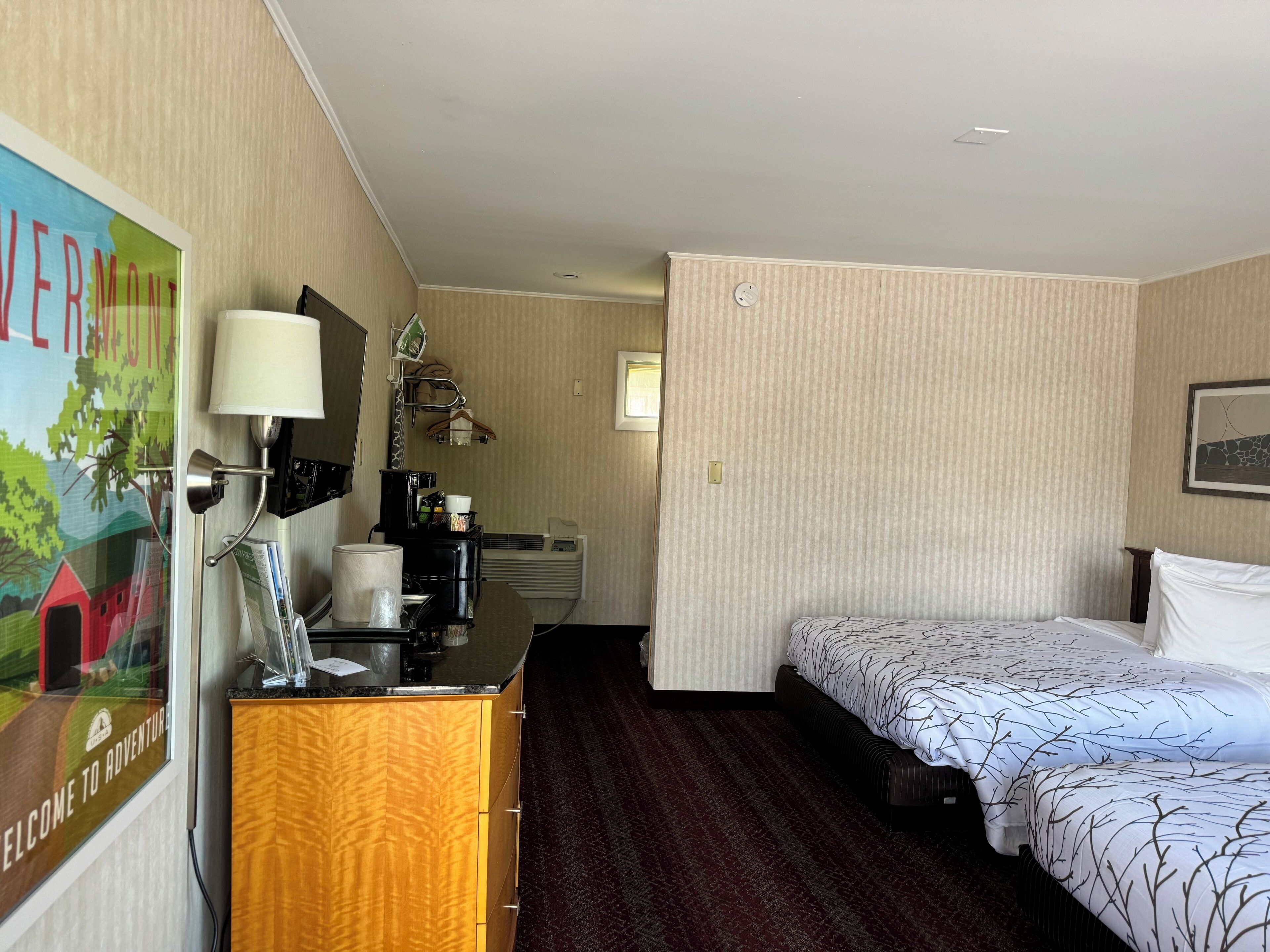 Ein Hotelzimmer mit einem Bett, einem Schreibtisch mit Lampe, einer Kaffeemaschine und einem Bild an der Wand.