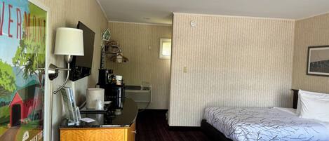 Ein Hotelzimmer mit einem Bett, einem Schreibtisch mit Lampe, einer Kaffeemaschine und einem Bild an der Wand.
