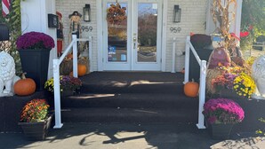 A building entrance with a white door, number 959, and a small porch area decorated with pumpkins, flowers, and scarecrows. - Black Mountain Inn (Brattleboro)