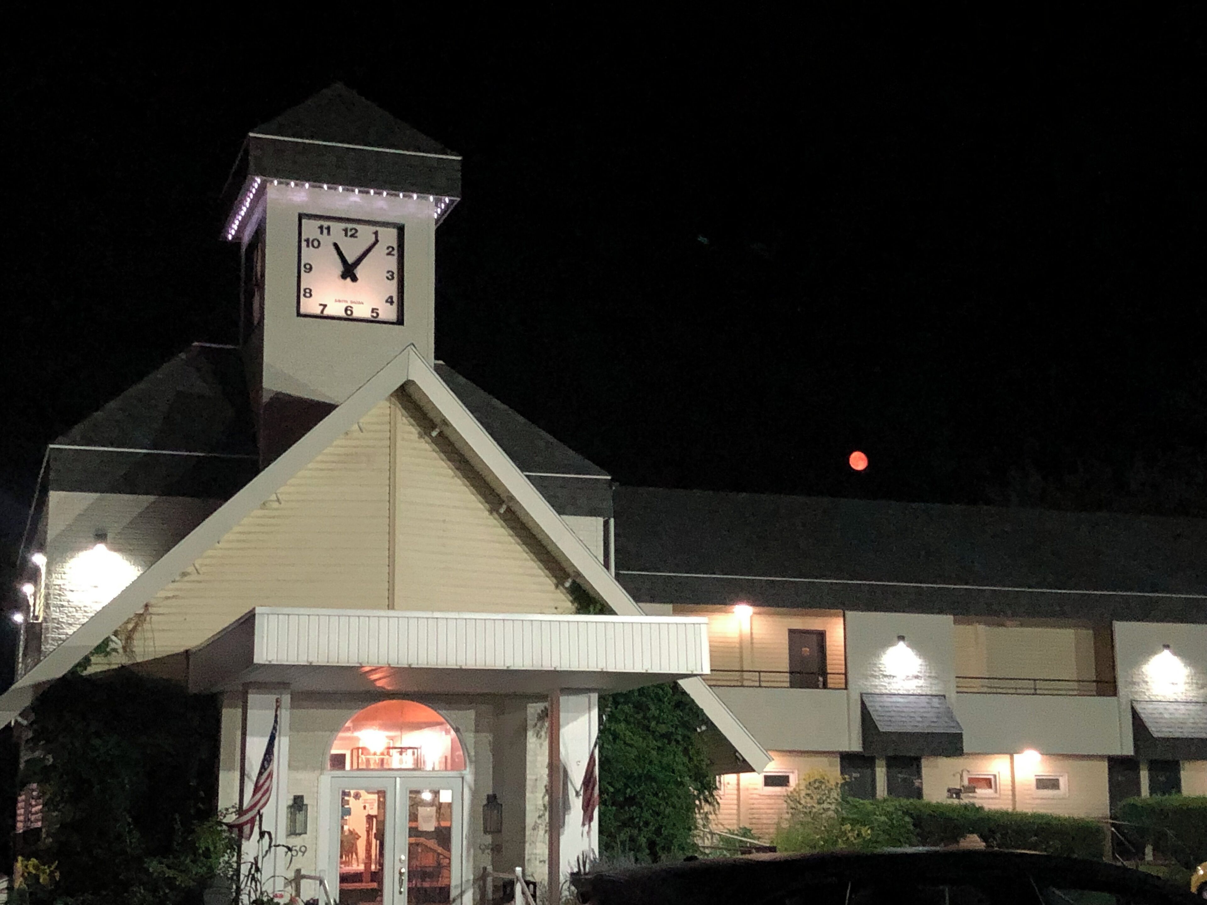 A building with a clock tower, a covered entrance, and a lit-up moon in the sky.