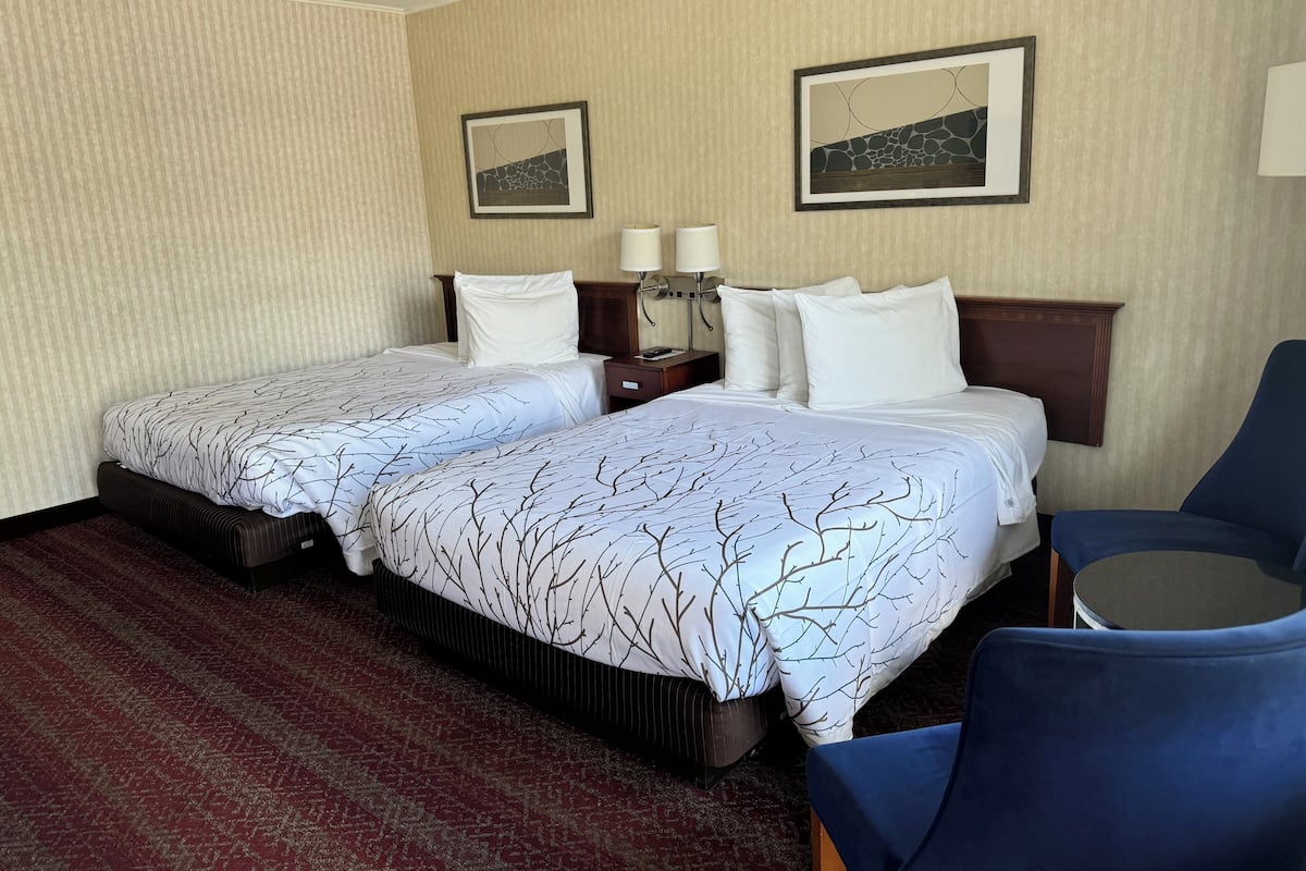 A hotel room with two beds, a desk, a chair, and two framed pictures on the wall.