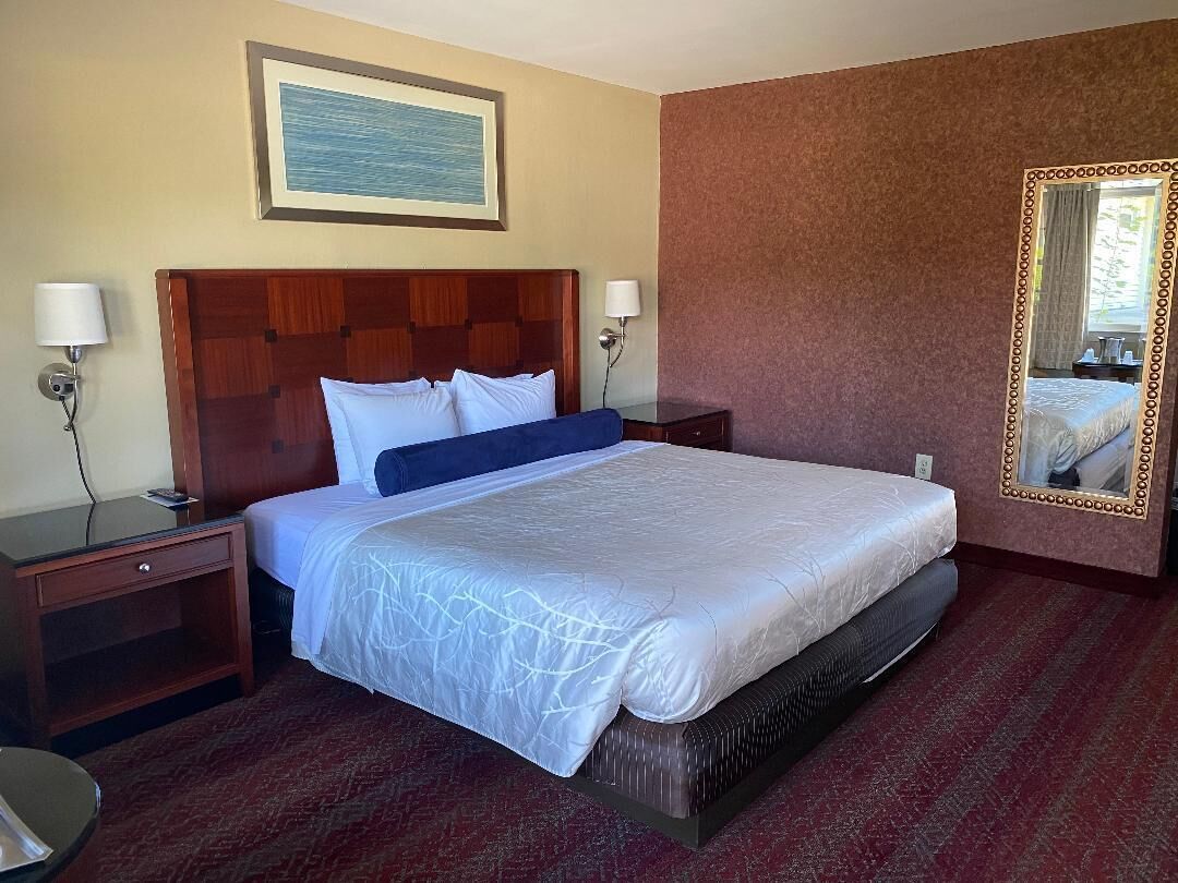 Ein Hotelzimmer mit einem großen Bett, zwei Nachttischen, einem Schminktisch, einem Spiegel und einem gerahmten Bild an der Wand.