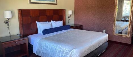Ein Hotelzimmer mit einem großen Bett, zwei Nachttischen, einem Schminktisch, einem Spiegel und einem gerahmten Bild an der Wand.