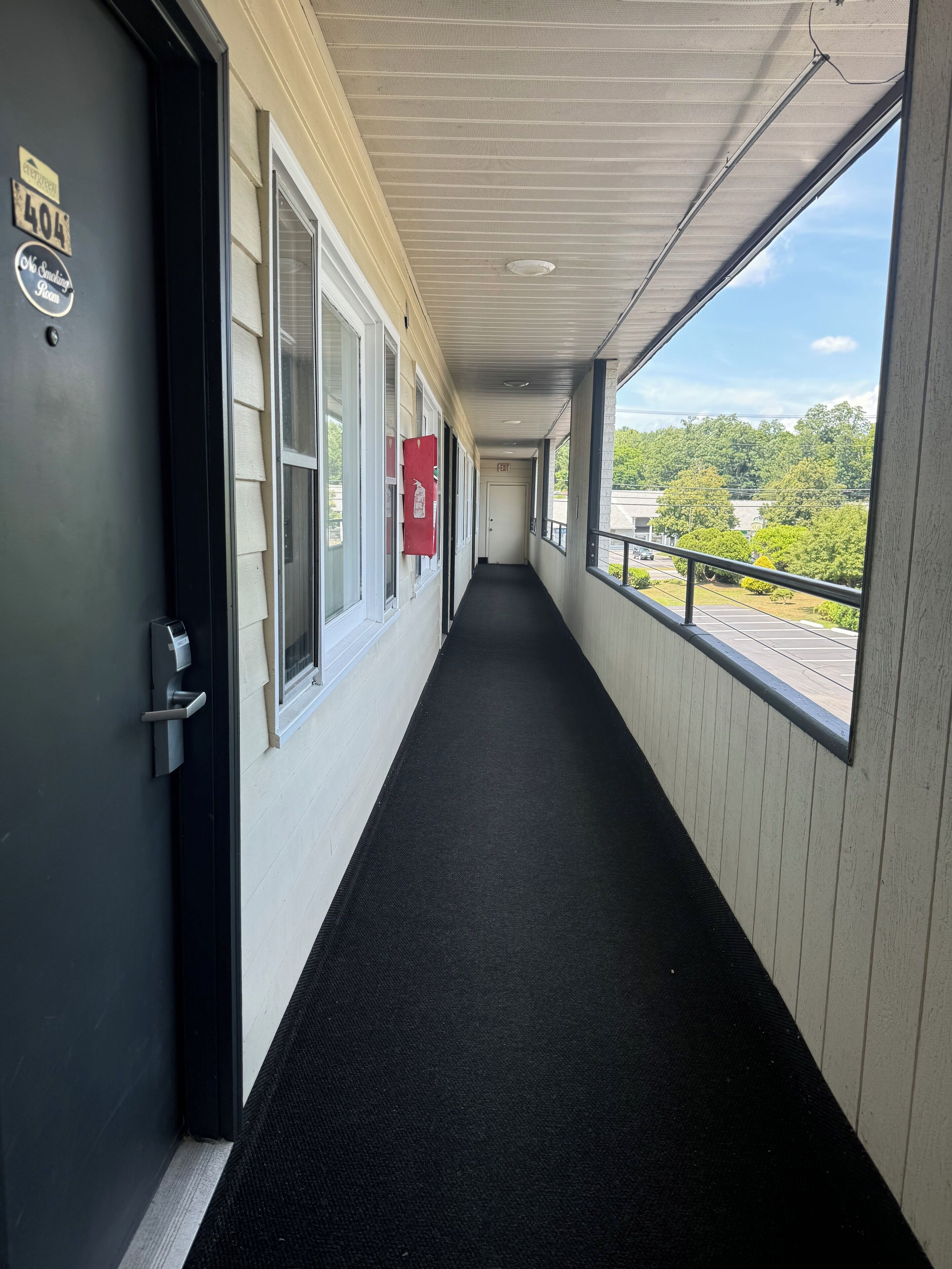 A hallway with a black carpet, a door marked "404", and a view of greenery outside.