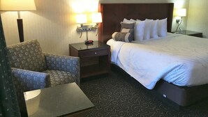 A hotel room with a bed, two bedside lamps, a nightstand, a chair, and a small table. - Black Mountain Inn (Brattleboro)