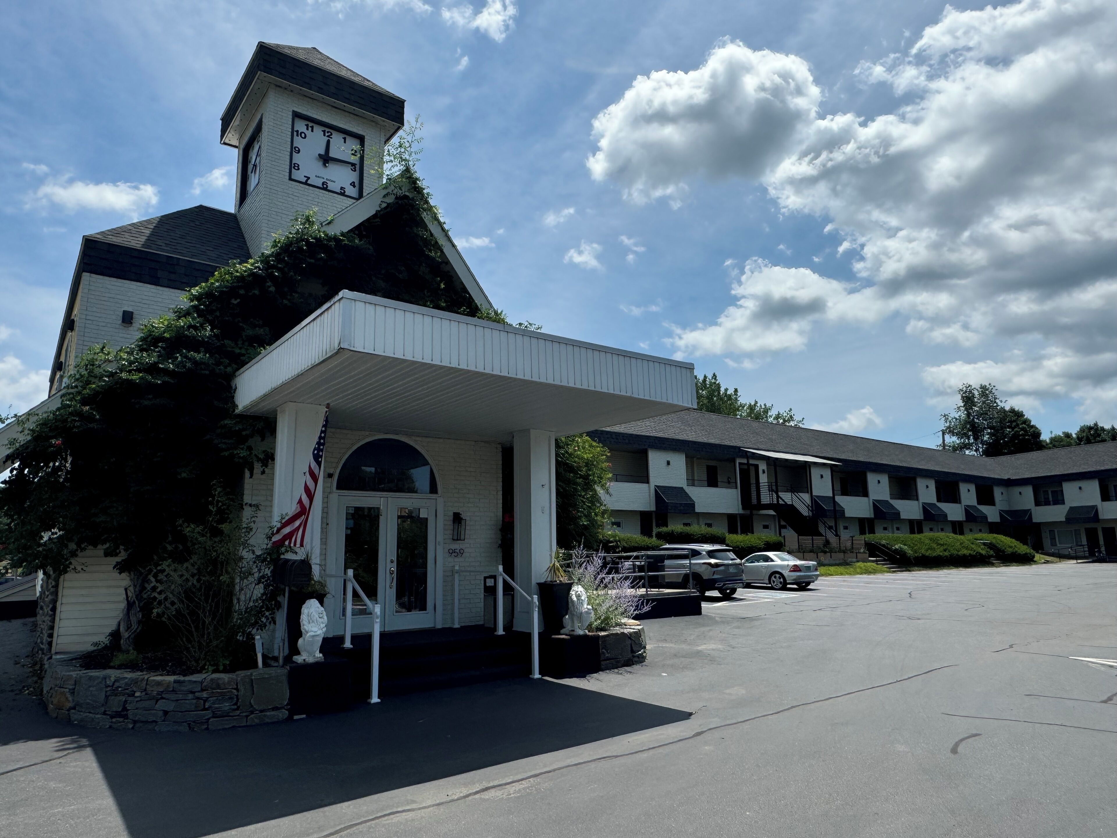 A building with a clock tower, a covered entrance, and a parking lot.