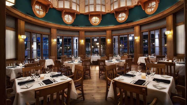 Un restaurant avec des tables rondes, des chaises en bois et de grandes fenêtres.