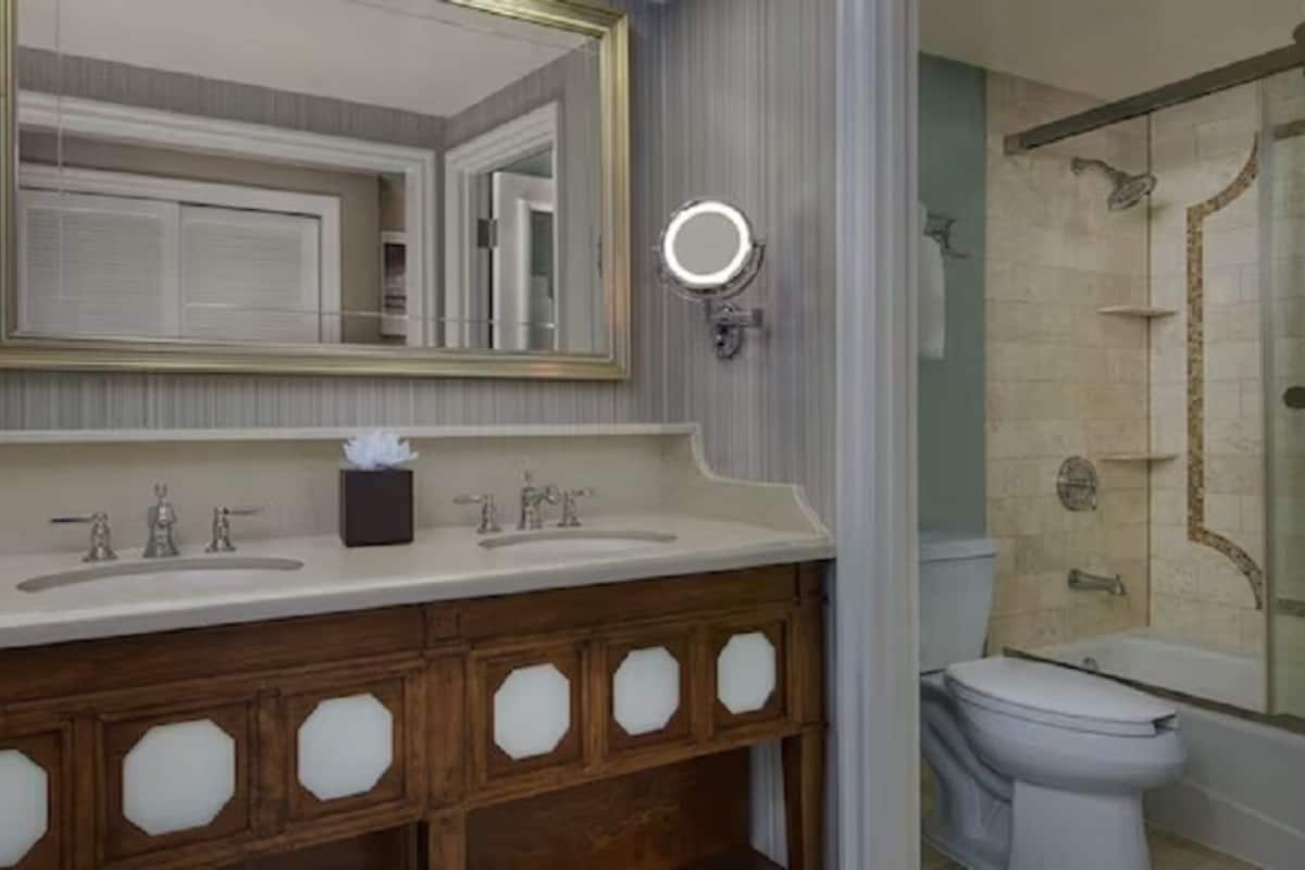 Un baño con tocador doble, espejo, cabezal de ducha de mano y retrete.